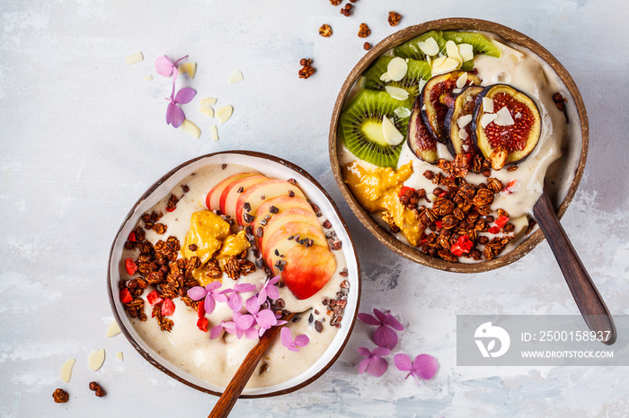 Smoothie bowl with fruit and granola with coconut shell bowl on gray background. Healthy vegan food concept.