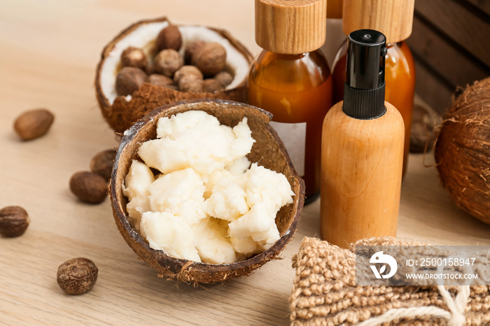 Coconut shell with shea butter an cosmetic products on wooden table, closeup