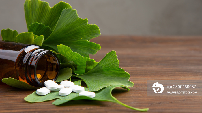 Bottle of pills and fresh ginkgo biloba leaves on wooden background. Traditional, herbal medicine and Homeopathy concept.