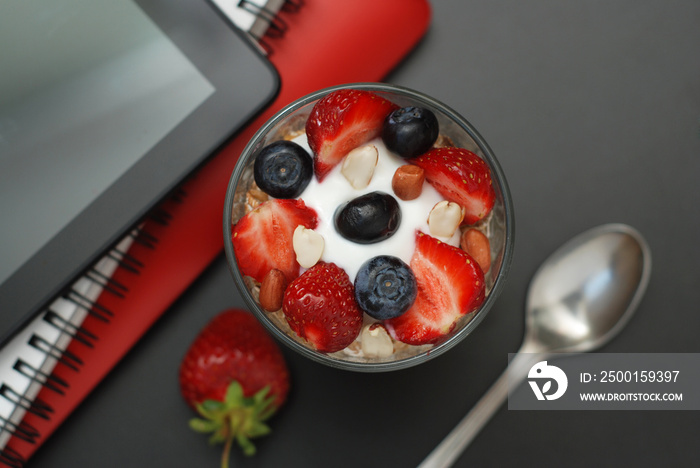 Breakfast for health, fresh strawberries, Blueberies, with oatmeal Black office table. Tablet, laptop and Notebook. Top view. Copy space