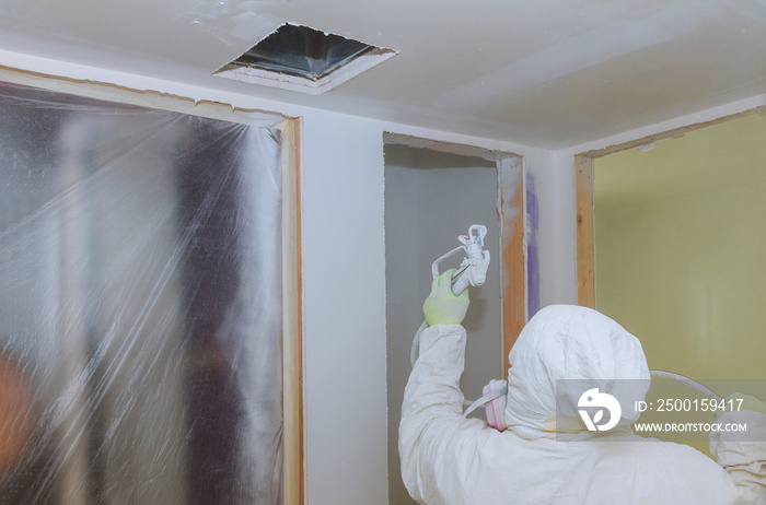 Worker painting wall with spray gun in white color.