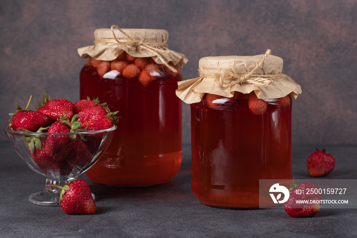 Homemade canned compote with strawberries in two jars on a brown background