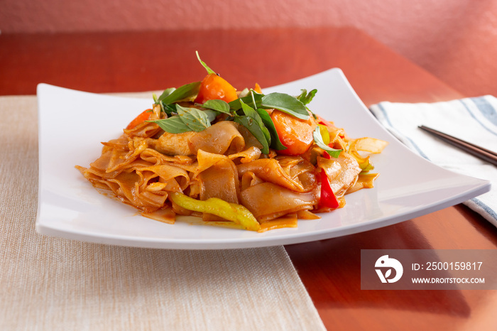 A view of a plate of drunken noodles in a restaurant or kitchen setting.