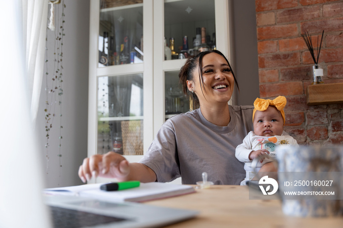 Smiling mother holding baby girl while studying at home