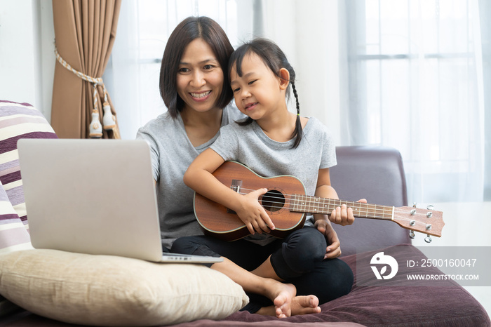 Asian mother and daughter using laptop studying to play ukulele at home