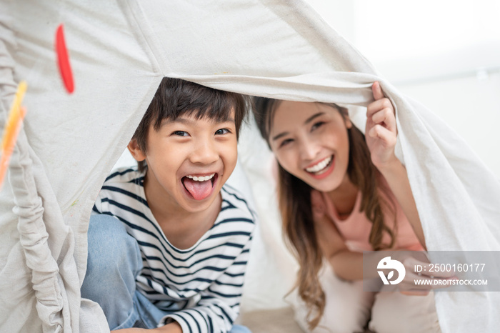 Happy mother and little son playing together in tent for children in living room at home