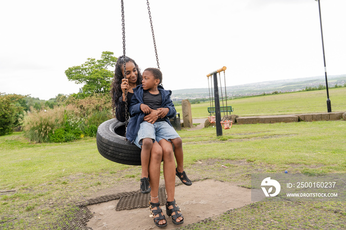 Mother and son swinging on tire swing at playground