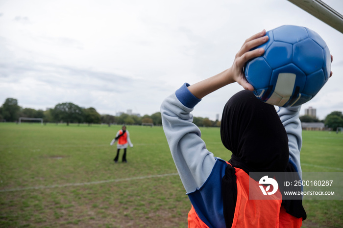 Two women in hijabs playing soccer in park