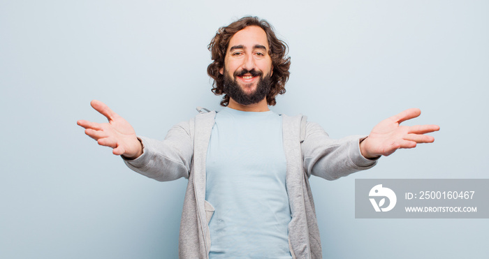 young bearded crazy man smiling cheerfully giving a warm, friendly, loving welcome hug, feeling happy and adorable against flat color wall