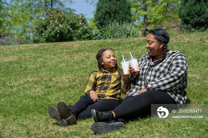 Mother and daughter (6-7) sitting in park and toasting with shakes