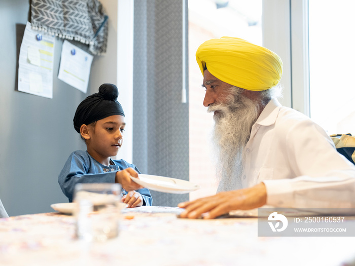 Grandfather and grandson (6-7) in traditional clothing setting table