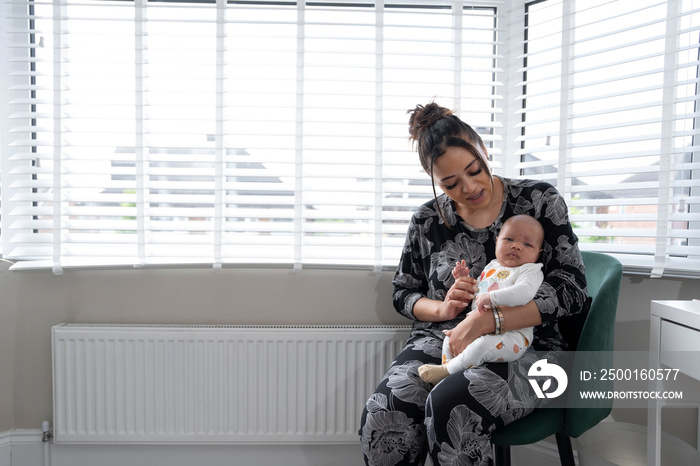 Mother sitting with newborn baby girl on chair at home