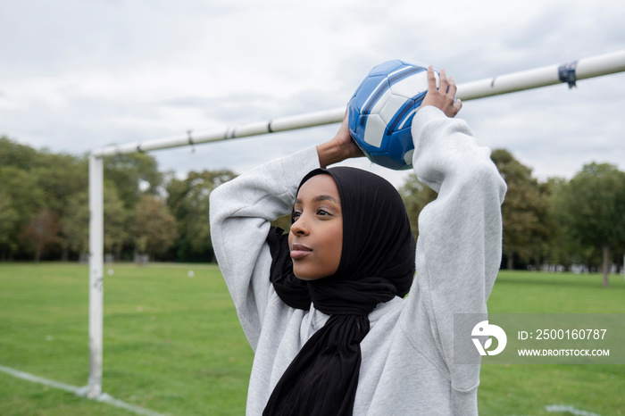 Smiling woman in hijab throwing soccer ball in park