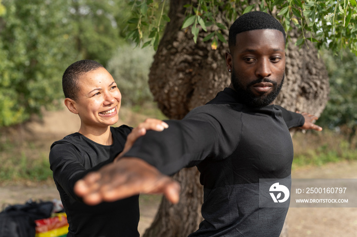 Yoga instructor assisting man practicing yoga in park