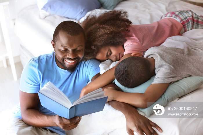 African American man reading bedtime story to his children at home