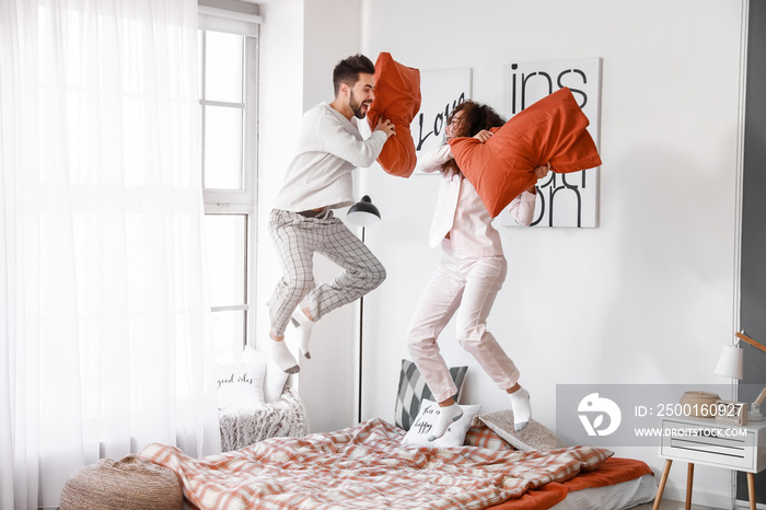 Happy young couple fighting on pillows in bedroom