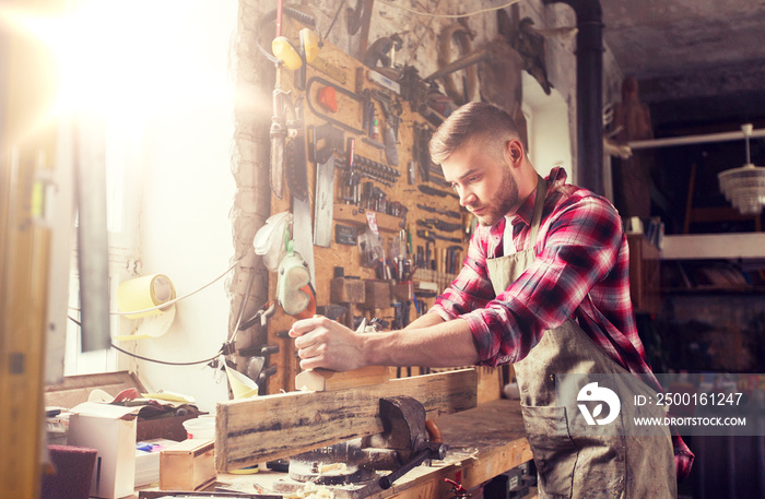 profession, carpentry, woodwork and people concept - carpenter working with plane and wood plank at workshop