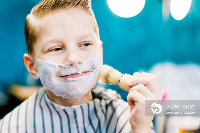 A closeup of a cute boy smearing his face with shaving gel.