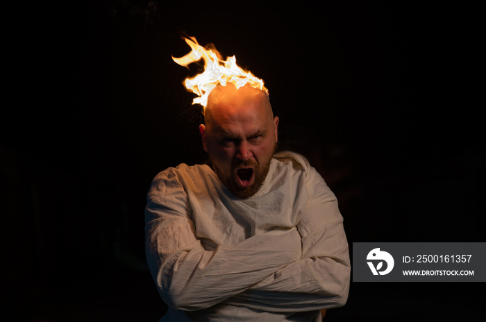 Bald man in a straitjacket with a burning head on a dark background.