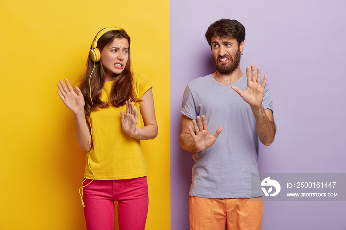 Displeased girlfriend and boyfriend make refusal gesture, feel aversion, smirk faces, dont like music, dressed in casual colorful clothes, isolated over yellow and purple background. Negative emotions