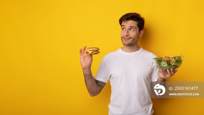 Portrait of Funny Young Guy Holding Burger And Salad