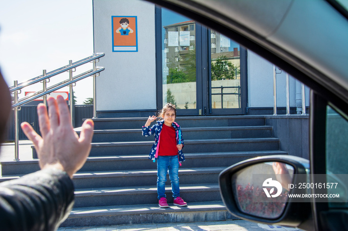 Little girl waving and winking at her father as her dad dropped him off at school