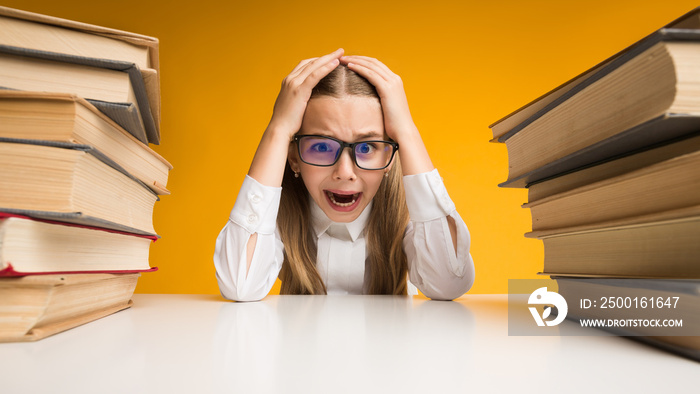 Stressed Elementary Schoolgirl Clutching Head Sitting Between Book Stacks