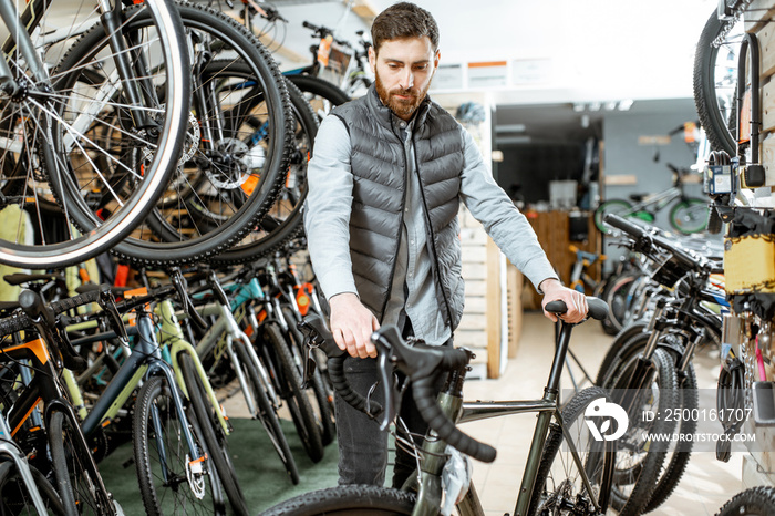 Man choosing new bicycle to buy standing in the shop with lots of bicycles and sports equipment indoors