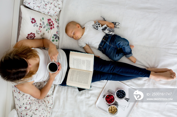 Mother and toddler baby boy, lying in bed, hugging with love, high angle shot, from above