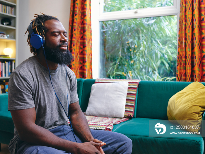 Man sitting on sofa, listening to music on headphones