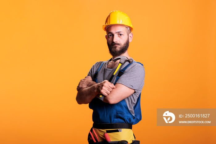 Craftsman engineer using hammer on renovation project, standing over yellow background. Professional male renovator doing reconstruction work with sledgehammer and tools, studio shot.