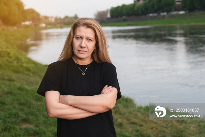 A woman against the background of nature, the river stands with a stern, slightly angry look, she needs to go home to cook, clean house, but she doesn’t want to, she wants peace and rest