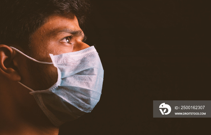 Young man wearing medical face mask to protect from spreading coronavirus outbreak infection in dark room and thinking of virus attack.