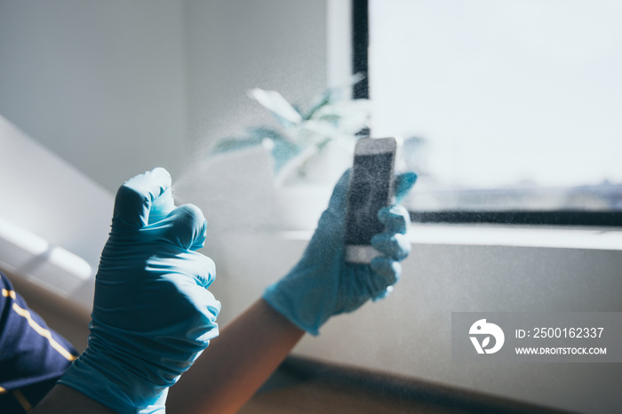 Close up young Asian man’s hand is spraying an alcohol spray to kill germs on smartphones, Initial protection against germs, Cleaning of electronic appliances or disinfectants during an epidemic.