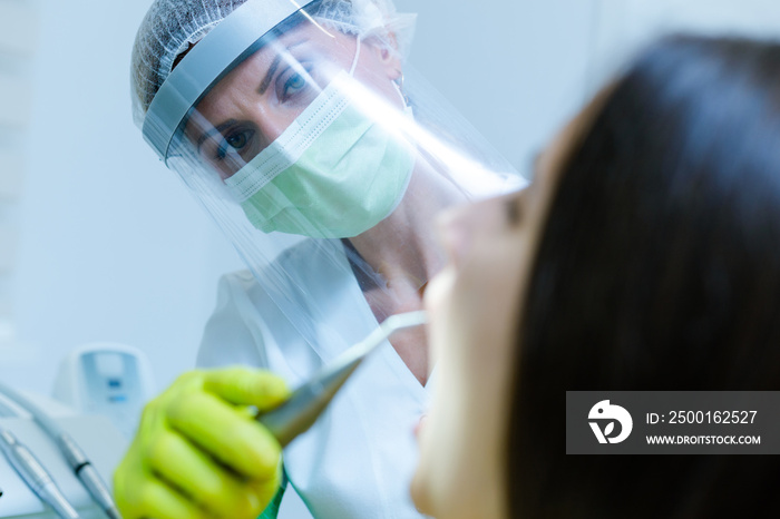 Female dentist wearing  face mask, gloves and visor as coronavirus safety precaution checkup dental health of young woman