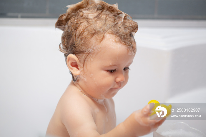 Washing adorable baby in bathroom. Kid with soap suds on hair taking bath. Closeup portrait of smiling kid, health care and kids hygiene. Child bubble bath.