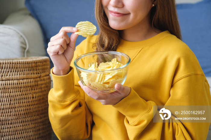 Closeup image of a young woman picking and eating potato chips at home