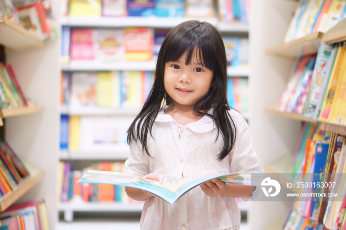 Asian children cute or kid girl reading and choose tale or story book on bookshelf in library or bookstore at school for learning and studying