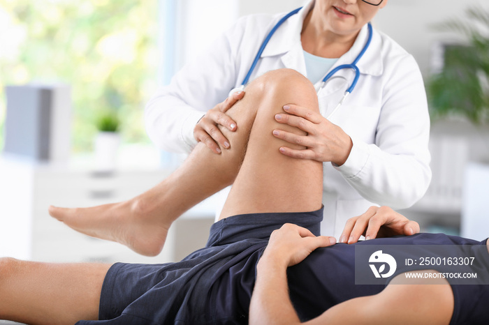 Mature doctor examining sportsman with joint pain in clinic