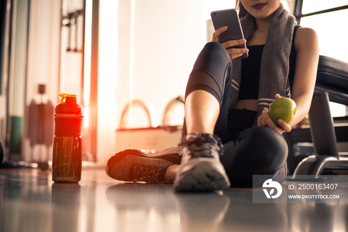 Close up of woman using smart phone and holding apple while workout in fitness gym. Sport and Technology concept. Lifestyles and Healthcare theme.