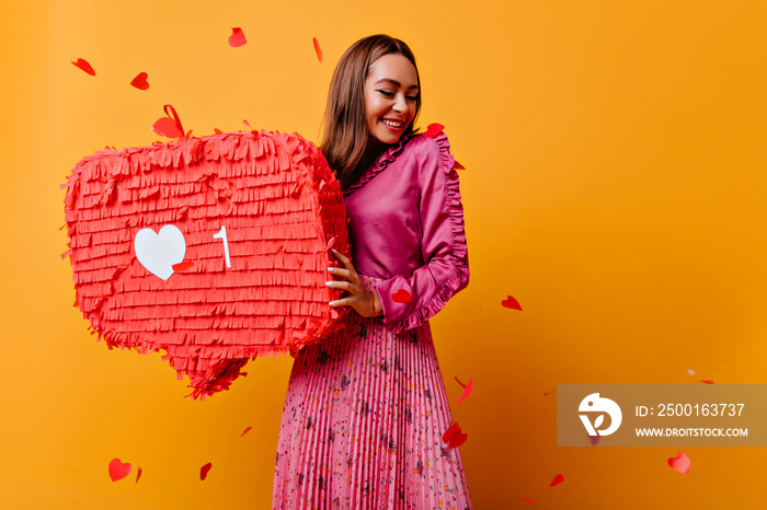 Cheerful girl with pretty smile posing with red bunner. Studio shot of refined brunette female blogger in good mood.