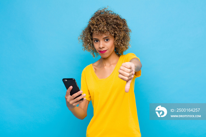 young african american feeling cross, angry, annoyed, disappointed or displeased, showing thumbs down with a serious look with a mobile phone