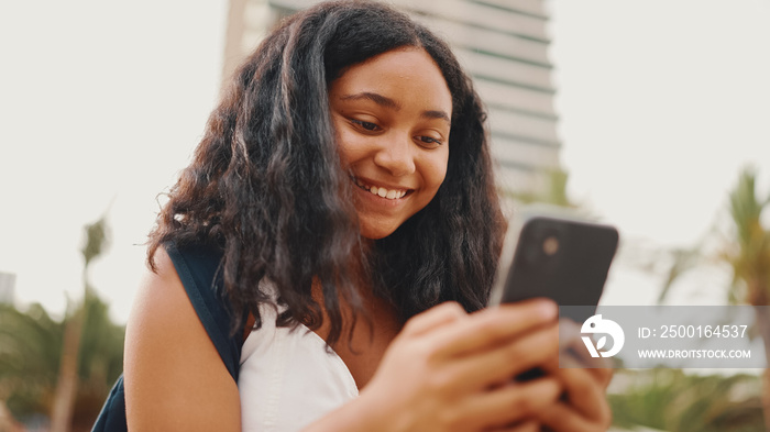 Pre-teenage girl uses mobile phone while sitting on the waterfront. Teenage girl making video call on smartphone