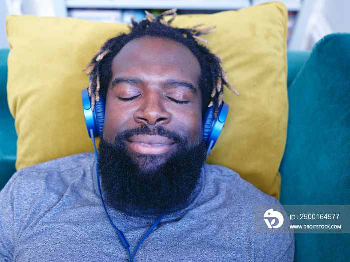 Man lying on sofa, listening to music on headphones