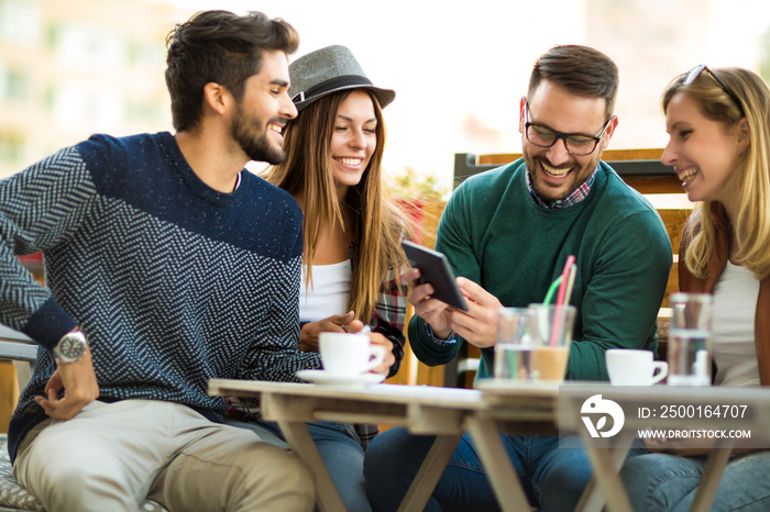 Group of four friends having a coffee together. Two women and two men at cafe talking laughing and enjoying their time using digital tablet.