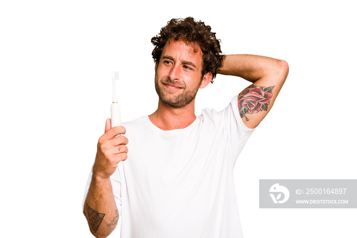 Young caucasian man holding an electric toothbrush isolated touching back of head, thinking and making a choice.