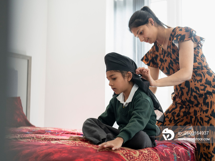 Mother wrapping traditional turban on son’s (6-7) head