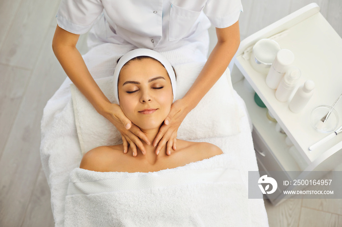 Hands of masseur making massage of face and neck for serene woman, top view