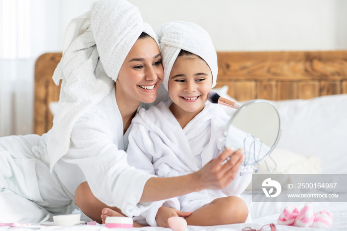 Mom tickling her cute little daughter with make up brush