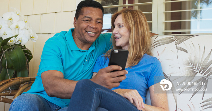 Smiling older couple sitting on porch and using cellphone together